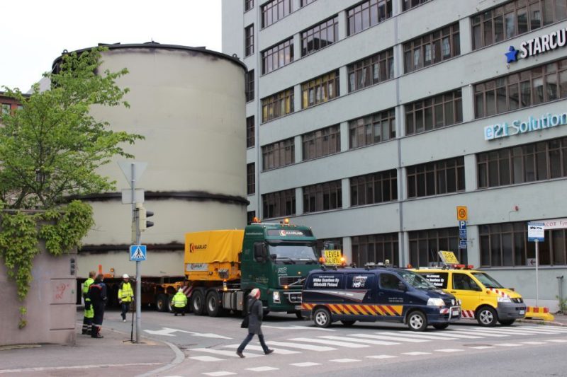 Suuri säiliö lavetilla kaupungin kadulla saattoautojen kanssa